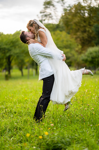 wedding couple, newly married bride and groom hugging and kissing outdoors on sunny summer day in natural meadow