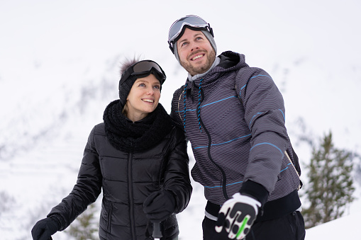 happy smiling skiing couple outdoors on ski piste on cloudy snowy winter day, waist up