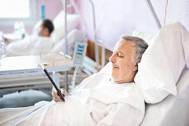 Middle aged man reading a tablet in a hospital bed stock photo