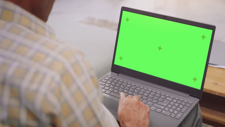 Over-the-Shoulder View of Elderly Indian Gentleman Using Laptop with Green Screen: Doing Remote Work, Virtual Meetings. Browsing Internet, Doing Online Shopping, Using Software. Template Chroma Key