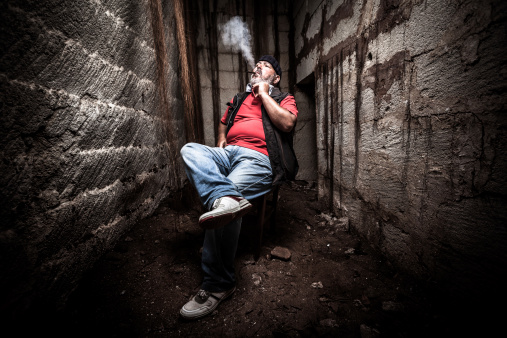 Senior man sitting in a dark location, smoking a cigar.
