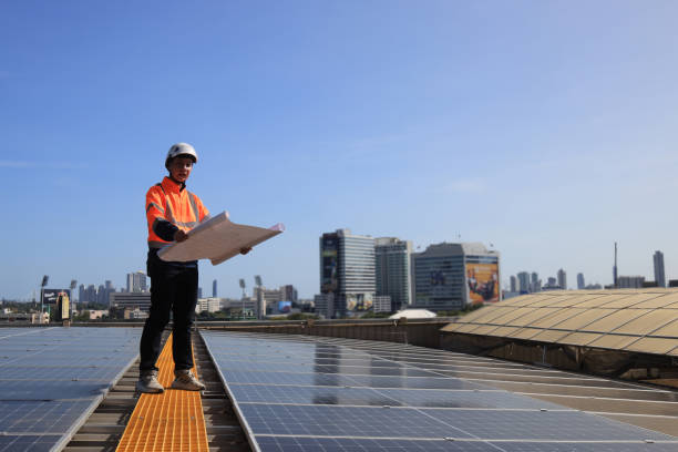 giovane ingegnere solare che indossa giubbotto di sicurezza arancione e elmetto bianco controllare il dettaglio sul disegno del progetto che lavora sul tetto solare - engineer environment orange manual worker foto e immagini stock