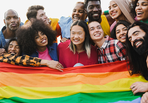 Crowd of multiracial people having fun together during LGBT pride parade outdoor - Diverse young friends from diverse cultures holding rainbow flag