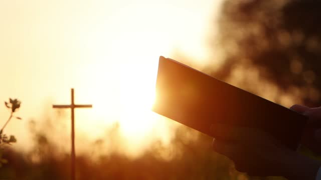 Beautiful sunset light, the cross of Jesus and Christian reading the Bible