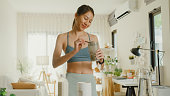 Young Asian athletic woman preparing protein shake at home. Diet and healthy food.