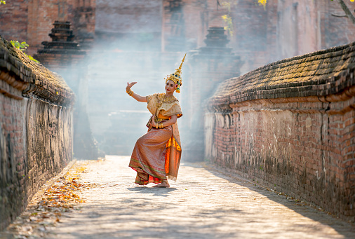 Asian beautiful woman with traditional dress dance with different actions on the way to ancient building and smoke or mist in the background with day light.