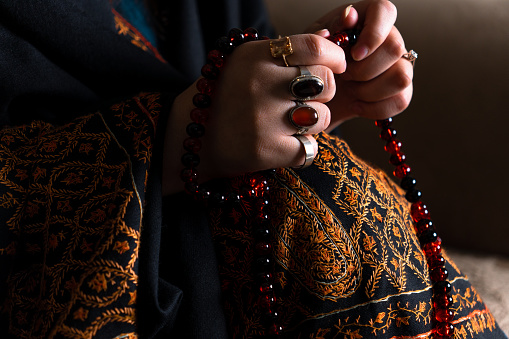 muslim women praying worshiping with beautiful glowing rosary tasbih counter in hand wearing gem stone rings religious spiritual practice dark and moody