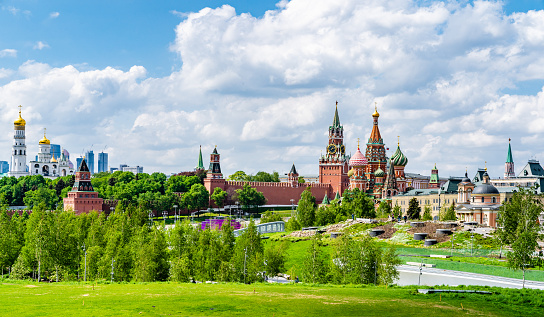 Picturesque view of the Moscow Kremlin, including the iconic Spasskaya Tower and St. Basil's Cathedral. The backdrop of the Moscow City skyscrapers adds a modern touch to the scene. The sky is blue, adorned with fluffy clouds, providing a serene atmosphere. Taken from Zaryadye Park, this image showcases the architectural beauty and historical significance of these landmarks in the heart of Moscow.