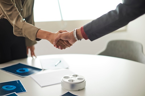 In a close-up shot that focuses solely on the hands, two businesspersons grip each other firmly in a handshake, signifying the successful closure of a  business agreement.