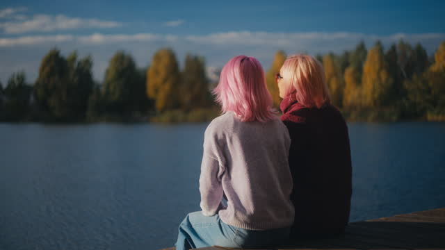 Happy pink-haired mother and daughter enjoying autumn scenery on the dock