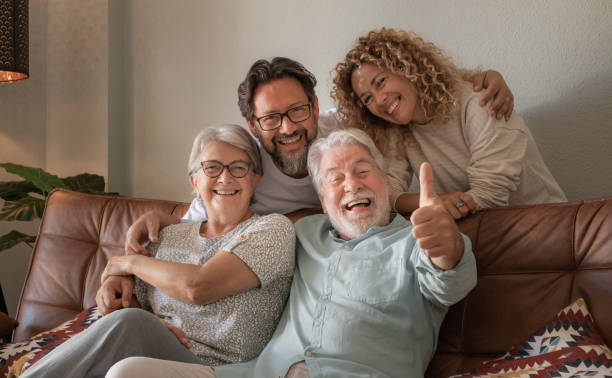 istock Happy multigenerational family group sitting on sofa at home laughing while spending time together. Four handsome bonding people, two generations looking at the camera 1491308518