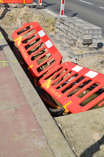 Wilsele, Vlaams-Brabant, Belgium -  May 18, 2023: sunny day, red white road works safety barriers fallen into an excavated hole, telecom cable repair infrastructure works along the road