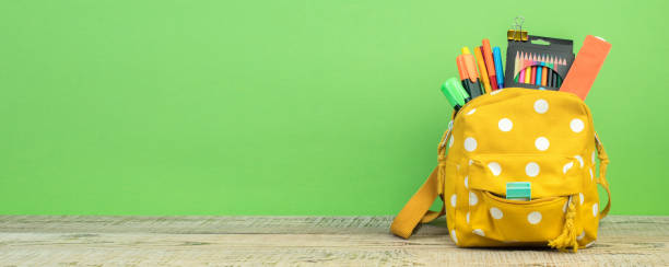 Yellow backpack with white polka dots with different colorful stationery on table. Bright green background. Back to school. Backpack with different colorful stationery on table. White background. Back to school. stapled paper stock pictures, royalty-free photos & images