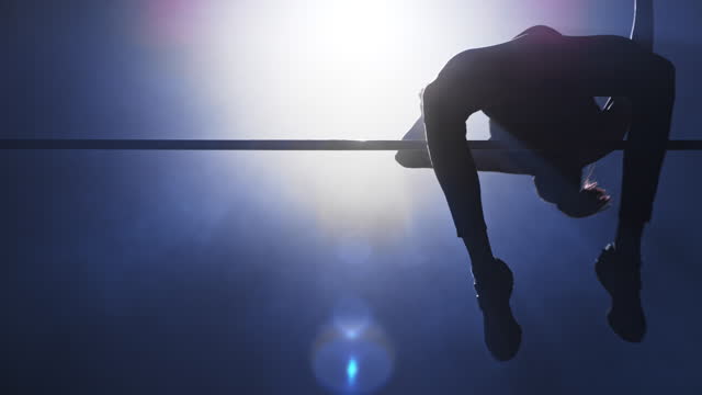 SLO MO LD High jump athlete jumping over the crossbar at night