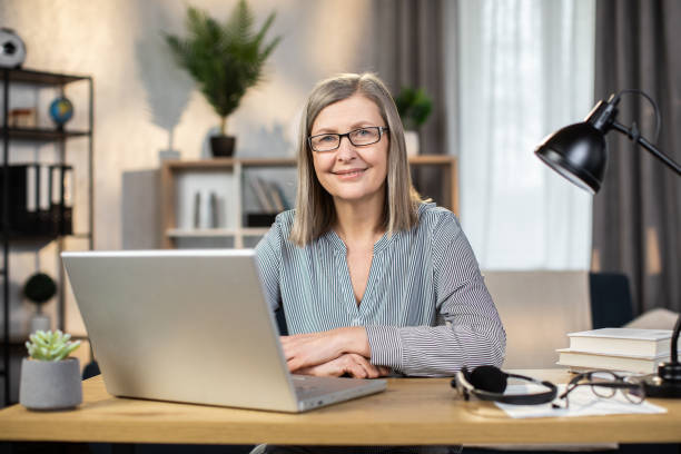 istock Mature lady posing with laptop at desk in remote office 1491313443