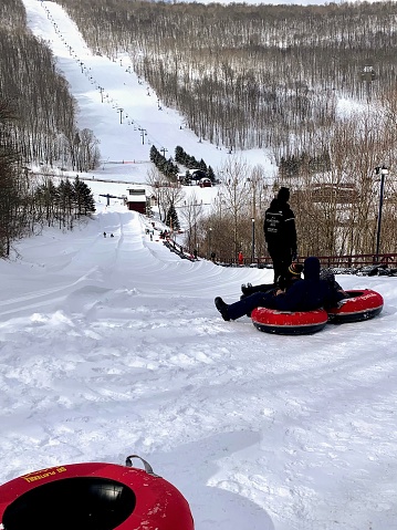 Roxbury, New York, USA February 20, 2021 A small family of three on top of Plattekill mountain sitting on snow tubes ready to slide down together. There are steep ski slops and other snow tubers.