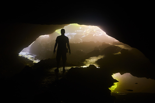 Image of Silhouette of person in cave opening over water