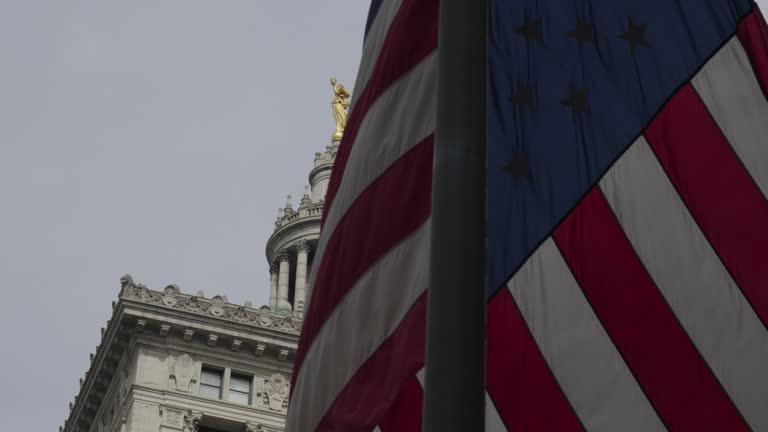 A gold statue of lady justice in the background is led by a billowing American flag