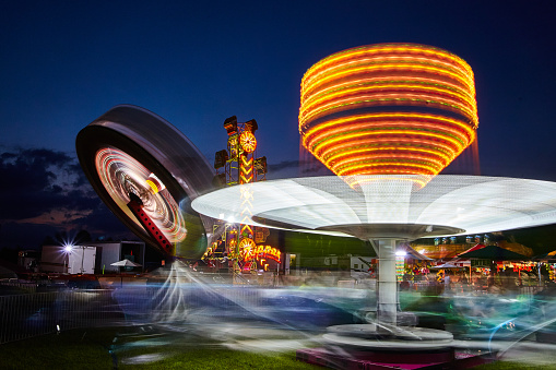 Image of Spinning rides and brilliant lights at a carnival or fair at dusk