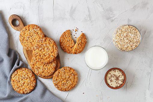 Oatmeal cookies with sesame seeds and flax seeds on a gray background with a jar of oatmeal and a glass of milk.
