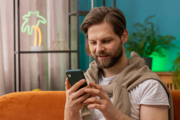 istock Caucasian young man sitting on sofa, using smartphone share messages on social media application 1491323808