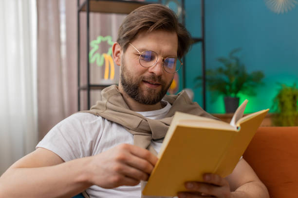 istock Young man relaxing interesting book turning pages smiling enjoying literature taking a rest on sofa 1491323819