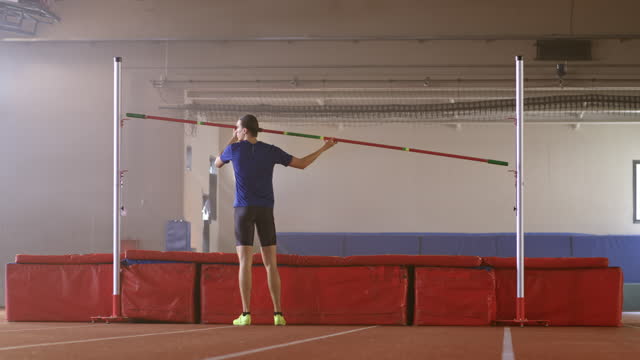 DS Wide dolly shot of a male athlete setting the height of the upright before high jump practice