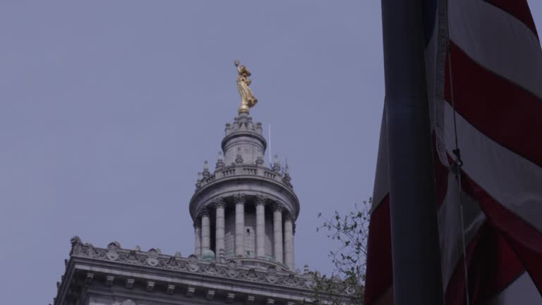 A gold statue of lady justice in the background is led by a billowing American flag