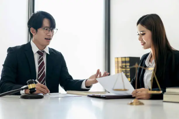 Female lawyer is discussing and legal advice about business contract documents to client while businessman is asking about laws and agreements of contracts in law firm office.