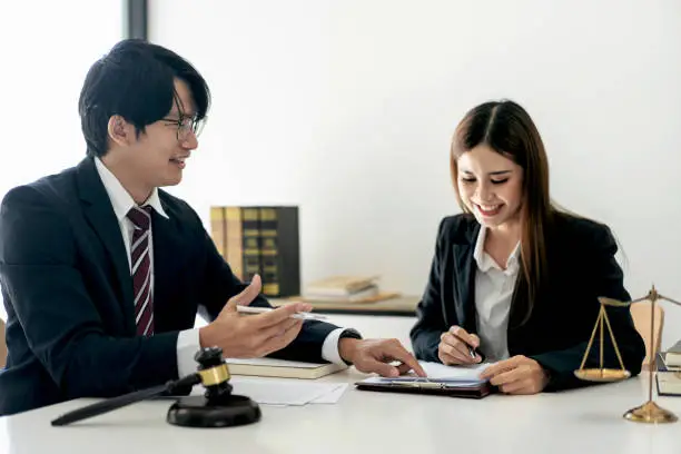 Female lawyer is discussing and legal advice about business contract documents to client while businessman is pointing on document and asking about laws and agreements of contracts in law firm office.
