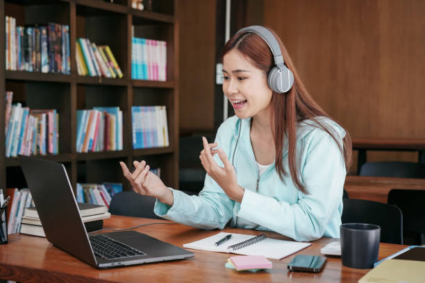 Female student wearing headphone and using laptop to asking ques Female student wearing headphone and using laptop to asking question with teacher on video conference in library while studying online learning to preparing for examination. online tutors stock pictures, royalty-free photos & images