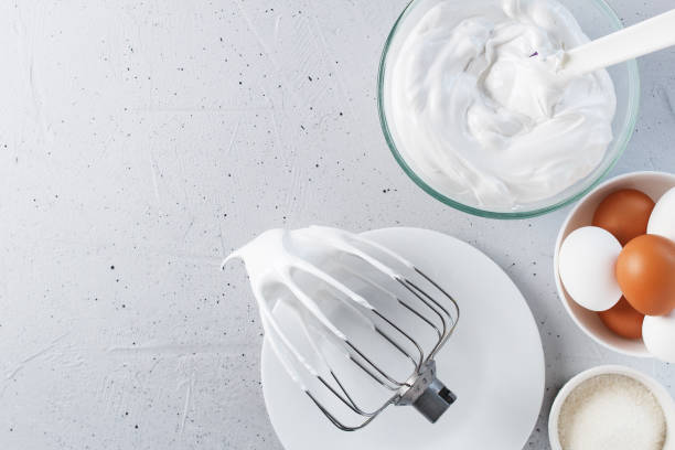istock Whipped egg whites - whipped Italian meringue on a wire whisk, eggs, sugar, on a gray background. copy space. 1491328209