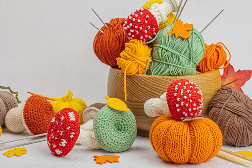 Set of clew of thread for knitting. Crocheted mushrooms, pumpkins, handmade, autumn hobby concept. Props and special craft tools on light stone concrete background, copy space
