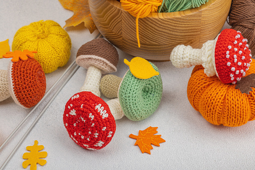 Set of clew of thread for knitting. Crocheted mushrooms, pumpkins, handmade, autumn hobby concept. Props and special craft tools on light stone concrete background, close up