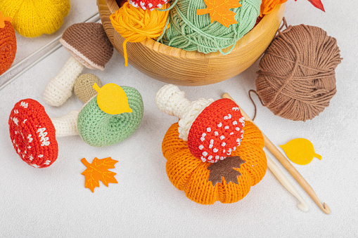 Set of clew of thread for knitting. Crocheted mushrooms, pumpkins, handmade, autumn hobby concept. Props and special craft tools on light stone concrete background, top view