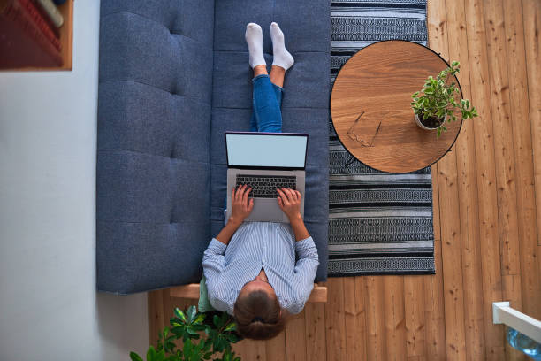 istock Woman freelancer sitting on the sofa and working remote on a laptop at home workspace. Top view 1491328513