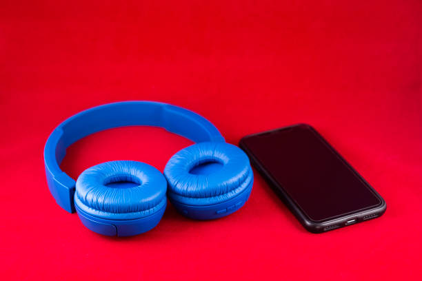 An elegant shot of a blue wireless headset and smartphone in a lightbox against a red background