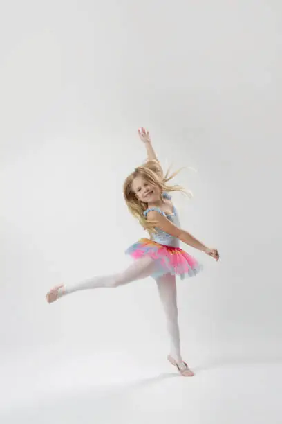 Studio portrait of beautiful little ballerina wearing colorful tutu skirt and pink ballet flats