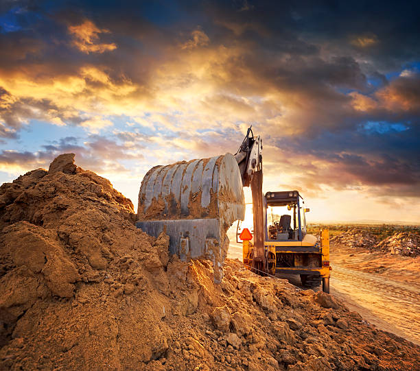 Excavator on the construction site of the road against the setting sun Excavator on road construction sand mine stock pictures, royalty-free photos & images