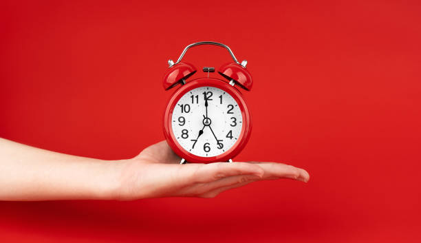 istock A woman's hand holds a red alarm clock against a red background 1491334810