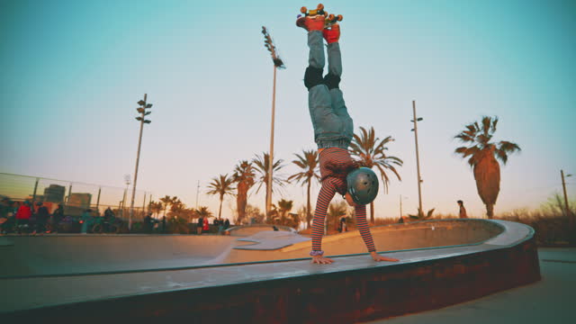 SLO MO of young female skater doing handstand against sky. Woman is practicing stunt while roller skating in city. She is at skateboard park.
