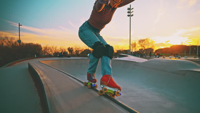 SLO MO of female skater practicing at sports ramp. Woman is doing stunt while roller skating against sky. She is at skateboard park during sunset.