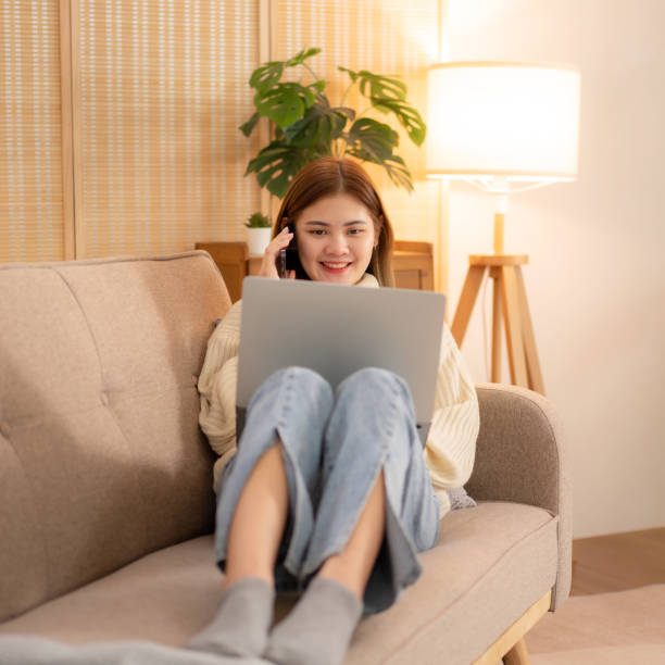 istock Young asian woman typing business data on laptop and talking with client on smartphone while wearing sweater 1491337724