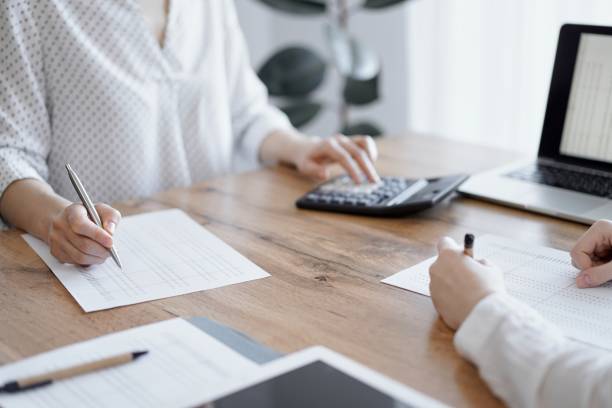 istock Woman accountant using a calculator and laptop computer while counting taxes with colleague at wooden desk in office. Teamwork in business audit and finance 1491339675