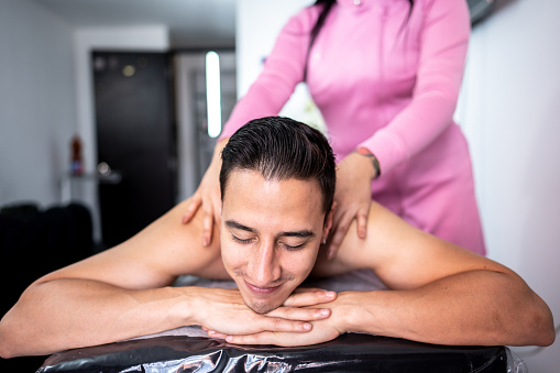 Mid adult man lying on front receiving massage on back at clinic