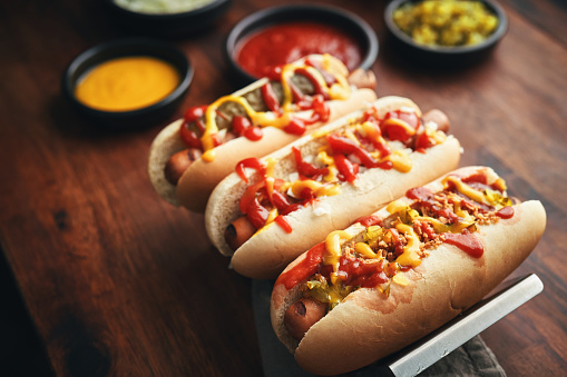 The photo depicts a mouthwatering assortment of Hot Dogs, each one customized with roasted onions, pickle relish and a variety of toppings.