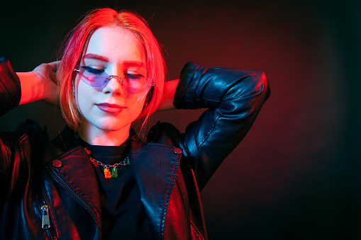 Studio portrait of a young white woman with brightly colored hair. in a black leather jacket and sunglasses