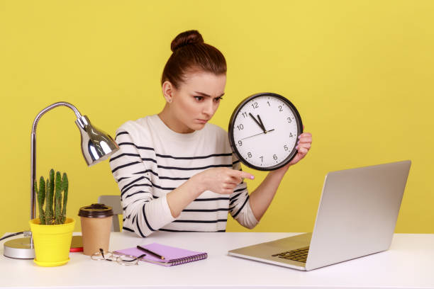 istock Woman holding big wall clock, time management, pointing to laptop screen with serious expression. 1491351107