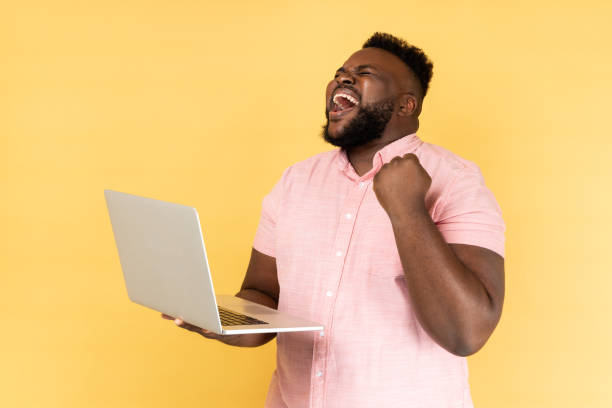 Extremely happy man screaming with joy and holding laptop, rejoicing victory, online betting. stock photo