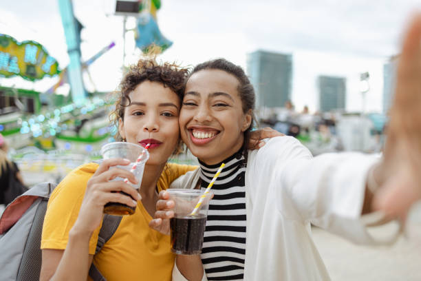 Cheerful multiracial women are feeling happy while drinking at the amusement park. They are looking at the camera and smiling.